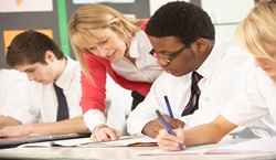 Teacher helping pupils in class with their writing